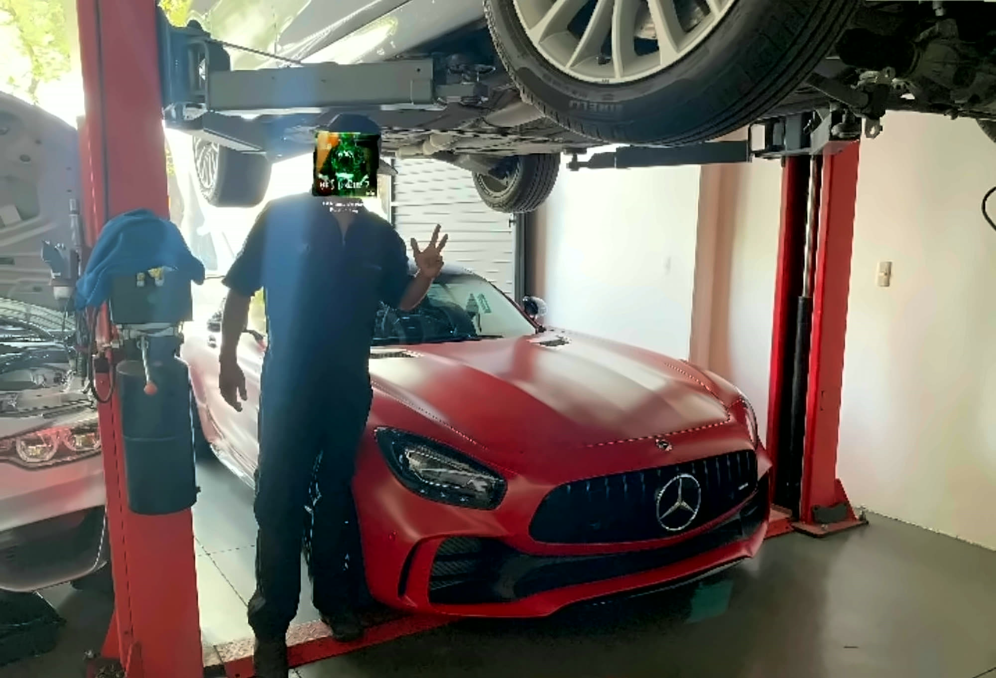 dR_Fg junto a un Mercedes-AMG GT R rojo mate en el elevador del taller